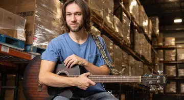 Christopher Capra holds a guitar with pallets of food behind him