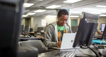 A student sits at a desk and types on a laptop computer