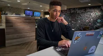 A student sits at a table at The Perk and is looking at a laptop screen