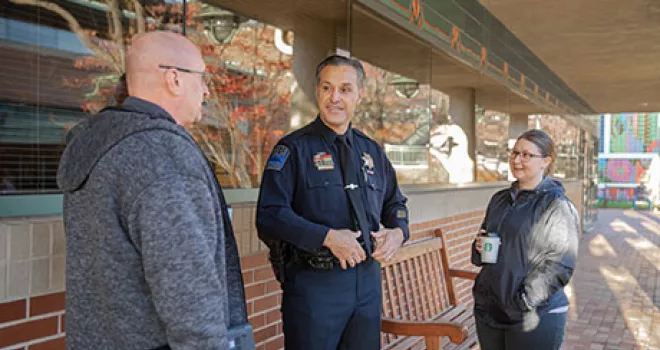 A police officer stands outside talking to two community members.