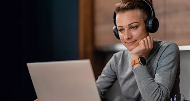 Female student sits at laptop and wears headphones