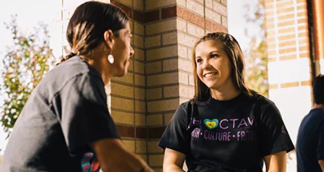 Two indigenous students talk while sitting on a bench.