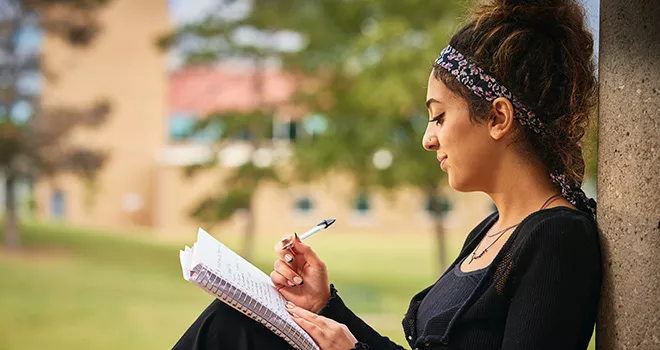 TCC student sits on campus and writes in her notebook.