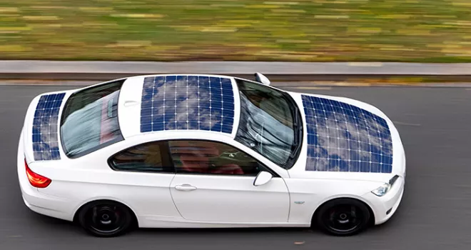 White car covered in solar power cells driving down the road at a high rate of speed.