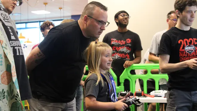 Cody Fimple looks on as Masyn Fimple uses a remote control to compete in a combat robotics match