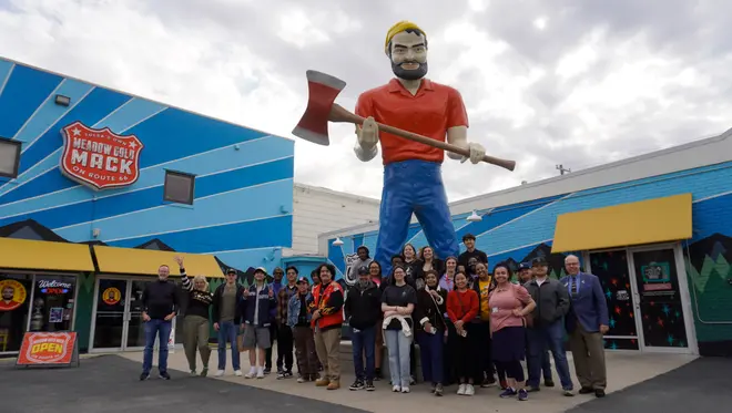 A group of about 30 TCC students, faculty, and community members stand in front of the Meadow Gold Mack statue.