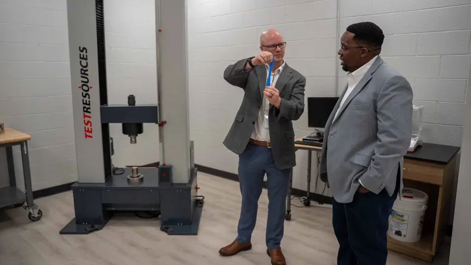 Dr. David Paige holds up a blue material lab while speaking with a man.