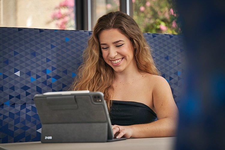 Smiling TCC student sits at a table and works on her tablet.